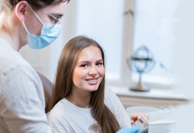 Junge Frau auf dem Zahnarztstuhl, blickt zufrieden in die Kamera.